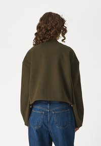 Dark olive green cropped sweater with a high neck and wide sleeves, paired with blue high-waisted jeans featuring a classic five-pocket design.
