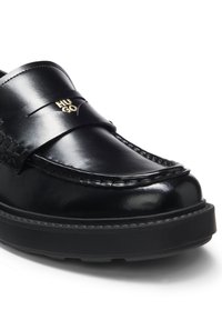 Mocassin en cuir noir avec une semelle épaisse et un détail du logo "HUGO" doré sur la lanière au-dessus de l’avant.