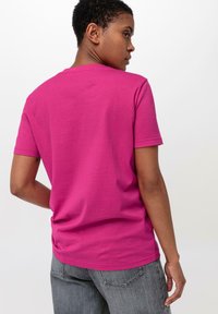 Fuchsia katoenen T-shirt met een ronde hals en korte mouwen, gedragen met grijze denim broek. Hie smooth textuur en nette stikdetails.