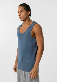 Blauw geribbeld tanktop met een ronde halslijn, mouwloos ontwerp en rafelige randen. De stof heeft een zachte textuur en een licht losse pasvorm.