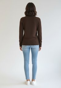 Brązowy sweter dzianinowy z fakturowanym brzegiem, noszony na jasnoniebieskich obcisłych dżinsach i białych trampkach, widziany od tyłu.