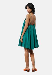 Robe sans manches teal à coupe ample, avec un dos froncé et des bretelles ajustables. Assortie à des mules orange avec un talon épais.