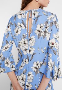 Floral dress with a light blue background, featuring white magnolia patterns, ruffled sleeves, and a keyhole back detail with ties.