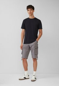 Czarny t-shirt z okrągłym dekoltem w komplecie z szarymi szortami cargo z bocznymi kieszeniami i sznurkiem. Białe sneakersy z czarnymi akcentami i szarymi podeszwami.