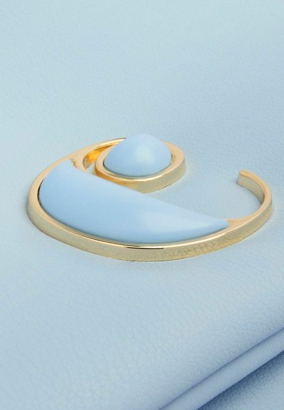 Zelta krāsas aplis pin ar gaiši zilu pusmēness un orbītas dizainu, kuram ir gludas un spīdīgas virsmas uz maigi zila fona.