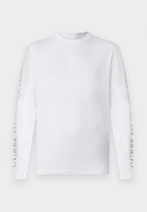 Hvid langærmet crew-neck skjorte med sort og rød tekst trykt lodret ned ad begge ærmer mod en ensfarvet baggrund.