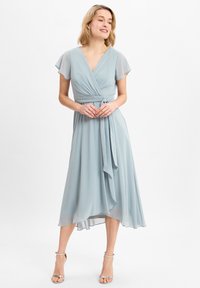 Lichtblauwe jurk tot de knie met een wikkelontwerp, korte, zwierige mouwen en een gestrikt taille-detail. Gemaakt van zachte, vloeiende stof.