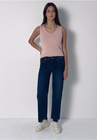 Ljust rosa ärmlös topp med V-ringning, kombinerad med mörkblå raka jeans och vita sneakers, med en minimalistisk design och mjukt tyg.