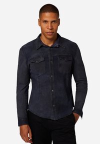 Mörk denimskjorta med knäppning fram, två bröstfickor, klassisk krage och långa ärmar. Slät textur med subtil blekning.
