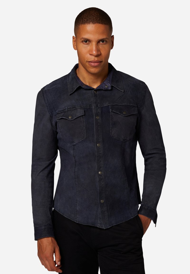 Mörk denimskjorta med knäppning fram, två bröstfickor, klassisk krage och långa ärmar. Slät textur med subtil blekning.