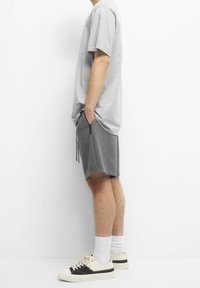 T-shirt en coton gris à manches courtes, associé à un short gris foncé avec poches latérales et cordons de serrage ajustables, porté avec des baskets basses.