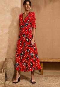 Rdeča obleka z V-izrezom, napihnjenimi rokavi in živalskim potiskom s pikami. Narejena iz lahkotnega materiala, ima oprijet pas in lepršavo krilo.