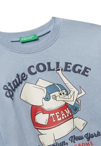 Hellblaues Shirt mit einem Cartoon-Elefanten, der ein rotes Trikot und einen blauen Helm trägt, mit dem Text "State College" und anderen hochschulbezogenen Wörtern.
