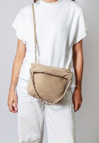 Borsa a tracolla in suede marrone con texture trapuntata, parte superiore pieghevole e una tracolla a catena. Presenta una forma morbida e arrotondata e un sottile dettaglio di cucitura.