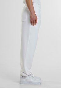 Witte sweatpants van zachte stof met een elastische tailleband, voorzien van een enkele zijzak en een taps toelopend ontwerp, gecombineerd met witte sneakers.