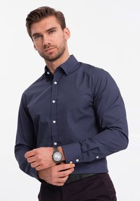 Camisa de botones azul marino con un patrón geométrico, hecha de una tela suave, con un cuello extendido y botones blancos.
