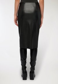 Gonna midi in pelle nera con una texture liscia e un design aderente, caratterizzata da una vita alta e un taglio dritto, abbinata a stivali neri al ginocchio.