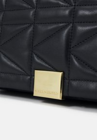 Sac en cuir matelassé noir avec une quincaillerie rectangulaire dorée portant le nom "KARL LAGERFELD". Surface texturée avec des coutures diagonales.