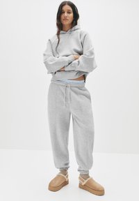 Šedá mikina s oversized rukávy, spárovaná s odpovídajícími šedými tepláky s elastickým pasem. Tanové boty s ovčí vlnou dokončují vzhled.