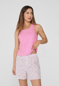 Světle růžový top bez rukávů v kombinaci s bílými šortkami s květinovým vzorem v růžové a modré barvě. Materiál vypadá měkký a prodyšný.