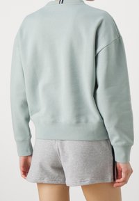Felpa blu chiaro con una vestibilità comoda, scollo tondo e polsini a coste, abbinata a pantaloni corti grigi con una striscia laterale nera.