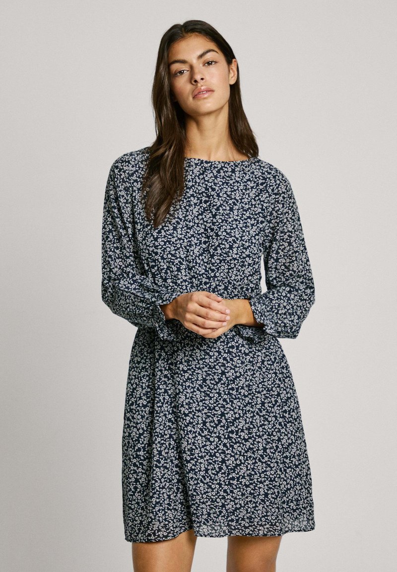 Marineblaues Kleid mit weißem Blumenmuster, langen Ärmeln, runder Ausschnitt und geraffter Taille. Leichter Stoff mit fließender Silhouette.