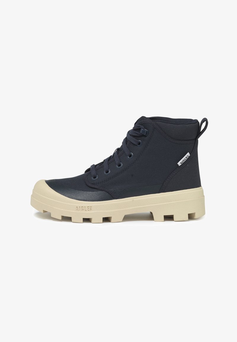 Bottines bleu foncé avec une tige texturée, semelles en caoutchouc crème et un motif de crampons distinctif. Présente des lacets et une tirette.