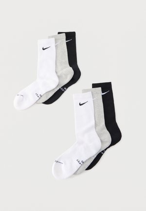 Δύο σετ από τρεις κάλτσες Nike σε λευκό, γκρι και μαύρο, τοποθετημένες επίπεδα σε ανοιχτό γκρι φόντο.