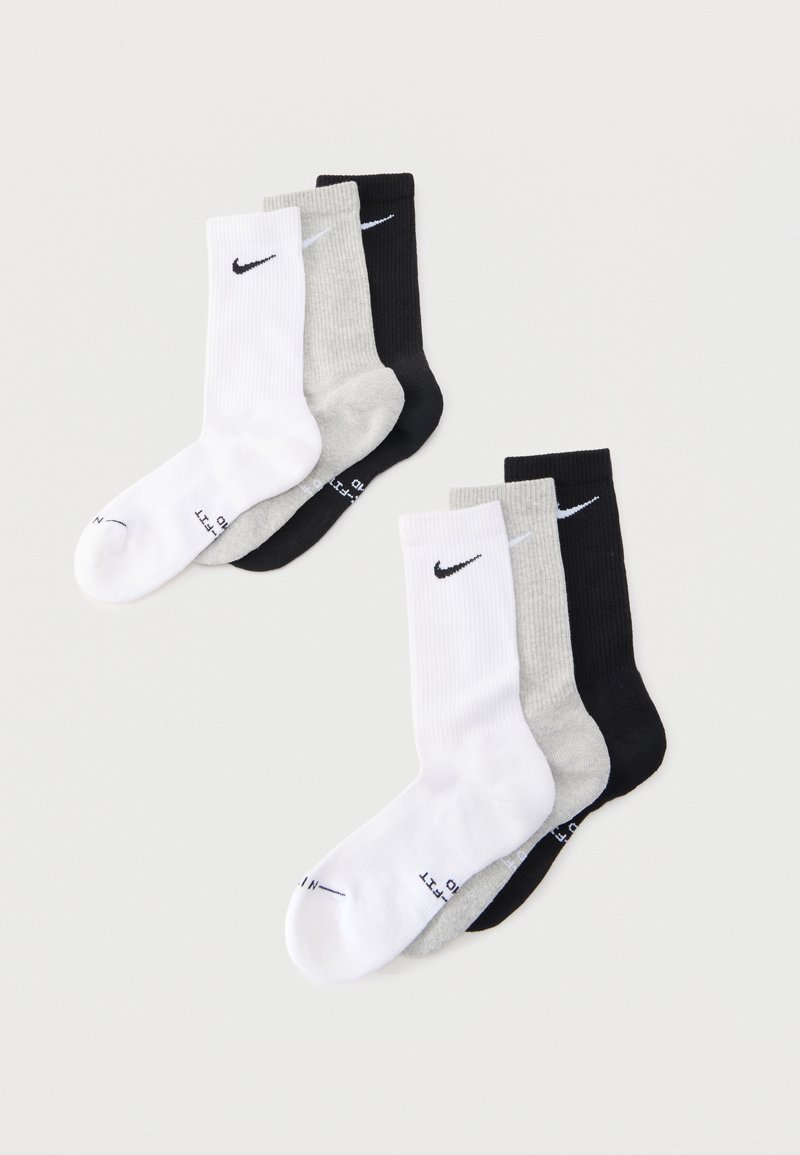 Δύο σετ από τρεις κάλτσες Nike σε λευκό, γκρι και μαύρο, τοποθετημένες επίπεδα σε ανοιχτό γκρι φόντο.