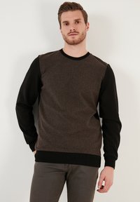 Brown and black knit sweatshirt with a textured body, solid black sleeves, ribbed neckline, and hem; minimalistic design.