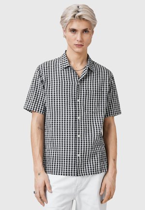 Black and white checkered short-sleeve shirt with a collar and front pocket, made of a lightweight fabric. Features button closure and sleek fit.