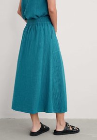 Teal, teksturoitu midi-hame, jossa on elastinen vyötärö ja sivutasku, yhdistettynä mustiin liukuhihnakenkiin, joissa on kaksi solkea.