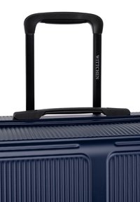 Valigia rigida blu navy con scanalature verticali, manico retrattile nero e impugnatura superiore. Presenta un marchio impresso sul manico.
