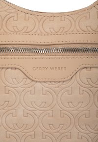 Bežová texturovaná kůže s embosovaným vzorem dvojitého G, stříbrný zip a prošitý štítek s embosovaným nápisem "GERRY WEBER" na přední straně.