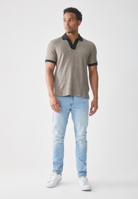 Grå polo skjorte med svarte detaljer, korte ermer og V-hals design. Kombinert med lyseblå jeans og hvite joggesko. Enkelt og uformelt utseende.