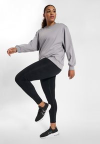 Grå sweatshirt med sportig design, svarta leggings med texturdetalj och svarta sneakers med vita sulor. Avslappnad atletisk outfit.