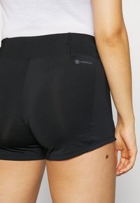 Pantalones cortos deportivos negros hechos de tela elástica, con una textura suave, cintura alta y un pequeño logotipo en la parte posterior.