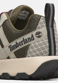 Tenisky Timberland s vrchní částí z pleteniny v olivové a krémové barvě, s logem na pásku, texturovanými detaily a černou gumovou podrážkou.