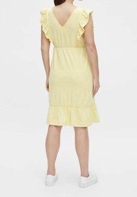 Abito giallo fino al ginocchio con maniche a volant e schiena a V. Presenta una vita arricciata e un orlo a strati. Indossato con sneakers bianche.