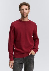 Rød crew neck sweater lavet af blødt materiale, med lange ærmer og en afslappet pasform. Parret med mørkegrå jeans.