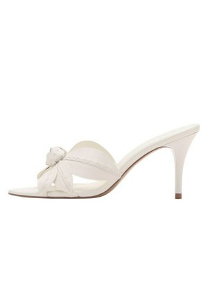 Sandalia mule blanca de tacón alto con puntera abierta, detalle decorativo de flor anudada en la tira y un tacón delgado de altura media.