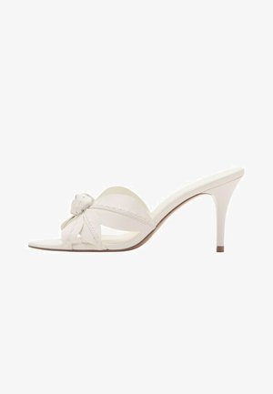 Sandale mule albe cu toc înalt, cu vârf deschis, detaliu decorativ în formă de floare înnodată pe bretea și toc subțire de înălțime medie.