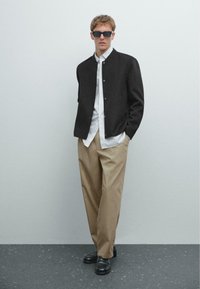 Dark wool jacket, white striped shirt, beige trousers, black loafers, and sunglasses. Slim-fit design with button closure and pockets.