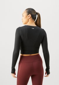 Zwarte lange mouwen crop top met een aansluitend ontwerp, gladde textuur en een eenvoudig logo op de achterkant, gecombineerd met hoog getailleerde bordeauxrode legging.