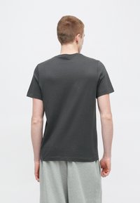 Tmavosivré bavlnené tričko s krátkymi rukávmi, okrúhlym výstrihom a pohodlným strihom, nosené so svetlosivými šortkami.