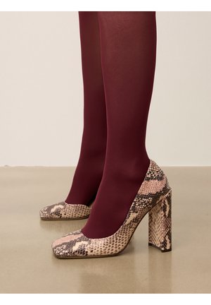 Zapatos de tacón alto con un diseño de estampado de serpiente en rosa y marrón, con puntera cuadrada y tacón grueso. Llevados con medias burdeos.