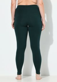Leggings verde scuro realizzati in tessuto elastico, con vita alta, texture morbida e design aderente che si restringe alle caviglie.