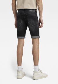 Black denim shorts with rolled cuffs, five-pocket design, and a brand patch on the waistband. Worn with white sneakers and crew socks.