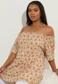 Blusa floreale off-shoulder con base crema e motivi rossi, arancioni e verdi, in tessuto leggero e maniche a vestibilità rilassata.