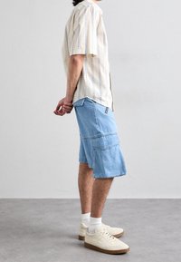 Short-sleeve striped shirt in cream and blue, paired with light blue denim cargo shorts and beige sneakers with textured accents.